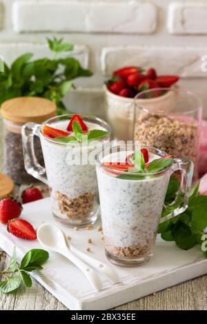Gesundes Essen Konzept Frühstück. Erdbeerparfait mit Joghurt, Chiasamen, hausgemachtem Müsli und frischen Beeren auf einer Steinbetonarbeitspfläche. Stockfoto