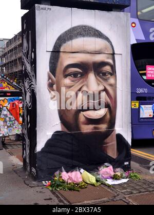 Blumen sind auf einem Wandgemälde von George Floyd, gemalt von Street Artist Akse, das vor kurzem in Stevenson Square, Central Manchester, England, Großbritannien erschienen gelassen worden. Floyd, ein afroamerikanischer Mann, starb am 25. Mai 2020 in Minneapolis, Minnesota, USA, während er von 4 Polizeibeamten verhaftet wurde, nachdem ein Verkäufer behauptet hatte, er habe versucht, mit einer gefälschten 20-Dollar-Rechnung zu bezahlen. Stockfoto