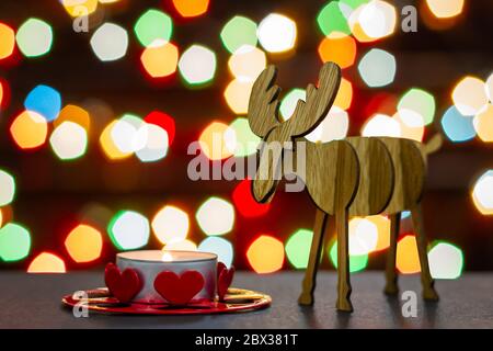 Elch Holzfigur und Teelicht Kerze auf Hintergrund von bunten Lichtern Bokeh. Selektiver Fokus. Stockfoto