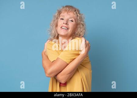 Entspannte reife Frau umarmt sich, erfreut freudigen Gesichtsausdruck Stockfoto