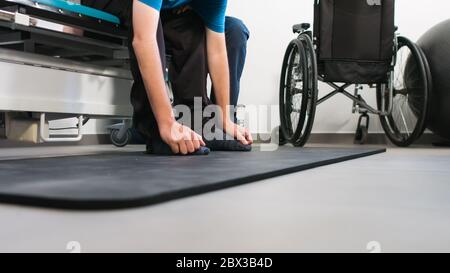 Physiotherapeut, der mit behinderten Menschen im Rollstuhl auf einem Therapietisch trainiert. Stockfoto