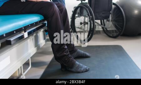 Physiotherapeut, der mit behinderten Menschen im Rollstuhl auf einem Therapietisch trainiert. Stockfoto