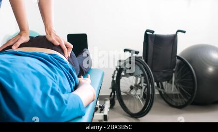 Physiotherapeut, der mit behinderten Menschen im Rollstuhl auf einem Therapietisch trainiert. Stockfoto