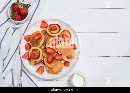 Draufsicht auf Mini-Pfannkuchen mit Erdbeeren auf weißem Holztisch. Gesundes Lebensmittelkonzept mit Platz für Text Stockfoto