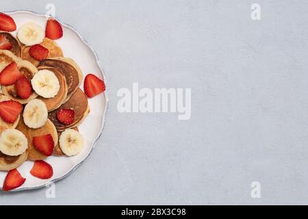 Hausgemachte kleine Pfannkuchen auf weißem Teller auf neutralem Betongrund. Bild mit Kopierbereich, Draufsicht Stockfoto