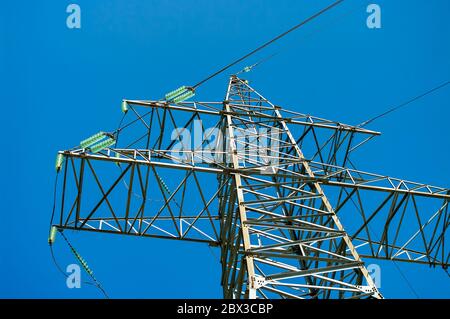 Hochspannungs-Sendebelst gegen blauen Himmel, Sonne und grüne Äste. Nahaufnahme Stockfoto