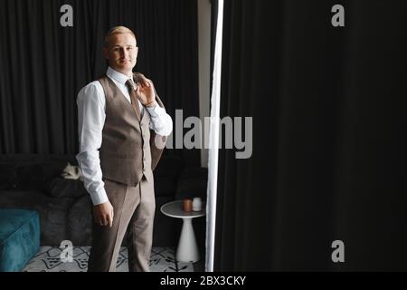 Mann im weißen Hemd, Weste und Krawatte, die die Jacke auf der Schulter halten, während sie im Zimmer stehen. Bräutigam Portrait Stockfoto