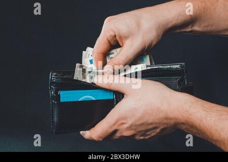 Mann Hand zieht Geld aus Geldbörse, schwarzem Hintergrund und schwarzer Geldbörse.2020 Stockfoto