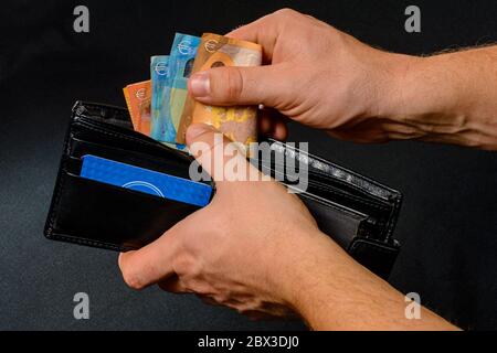 Mann Hand zieht Geld aus Geldbörse, schwarzem Hintergrund und schwarzer Geldbörse.2020 Stockfoto