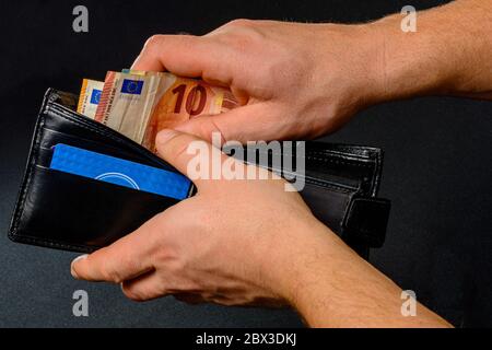 Mann Hand zieht Geld aus Geldbörse, schwarzem Hintergrund und schwarzer Geldbörse.2020 Stockfoto