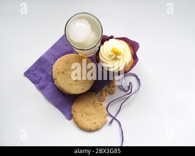 Draufsicht auf EINEN Cupcake, Kekse und ein Glas Limonade auf weißem Hintergrund, London, Großbritannien Stockfoto