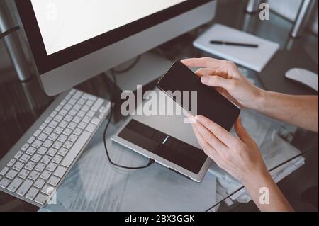 Weibliche Hände mit Smartphone im Innenbereich, freiberufliche Geschäftsfrau mit Handy am Schreibtisch, von zu Hause aus mit Smartphone und Stockfoto