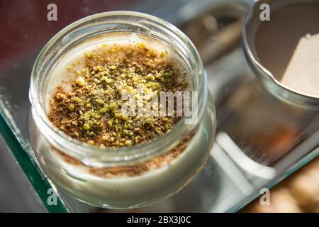 Draufsicht auf eine Schüssel Sutlac (Sütlaç) - traditionelle türkische aromatische Dessert, cremigen Reisbrei mit Zimt und Pistazien, serviert über einem schwarzen an Stockfoto
