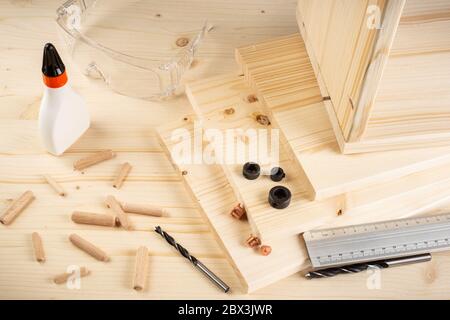 Holzdübel Fugenstifte Bohrer Leim Holzbohlen Sicherheitsgläser und Werkzeuge auf Fichte Hintergrund. Möbelbau-Konzept der Tischlerindustrie. Stockfoto