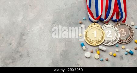 Doping für Sportler. Gold-, Silber- und Bronzemedaille und Kapseln auf grauem Hintergrund. Stockfoto