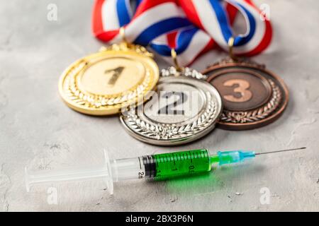 Doping für Sportler. Goldmedaille, Silber- und Bronzemedaille und Dotierspritze auf grauem Hintergrund. Stockfoto