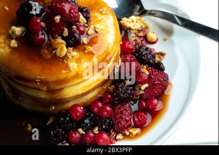 Nahaufnahme von Pfannkuchen mit Waldfrüchten Beeren auf Holztisch.Blaubeeren, Himbeeren auf Pfannkuchen mit Ahornsirup. Konzept Morgen Protein Frühstück Stockfoto