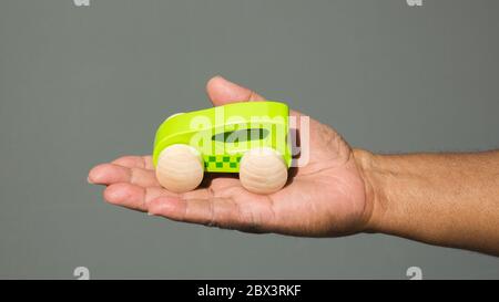 Die ausgestreckte Hand eines schwarzen Mannes mit der Handfläche nach oben hält ein grünes Spielzeugauto vor einem soliden Hintergrund mit Kopierfläche Stockfoto