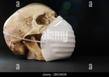 Isolierter Schädel vor einem schlichten dunklen, schwarzen Hintergrund, der eine einfache Papiermaske zum Schutz vor Geruchssgasen, Krankheiten oder Viren trägt. Covid-19 corona Stockfoto