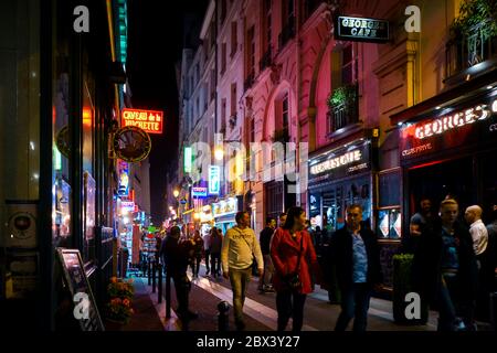 Touristen passieren Geschäfte und Cafés, während sie spät in der Nacht durch die bunten neonbeleuchteten Straßen im Quartier Latin in Paris gehen Stockfoto