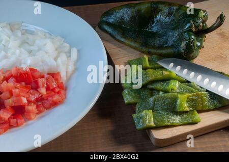 Chili poblano oder chili ancho, geschält und in Scheiben mit Zwiebeln und Tomaten auf der Seite, auf einem Holzbrett, Poblano Pfeffer oder Pasilla Pfeffer Stockfoto