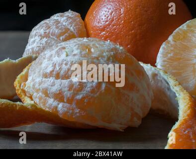 Scheiben aus geschälten Orange und Orangenhaut auf einem rustikalen Holztisch mit einem Rand Licht auf einer Orange Stockfoto