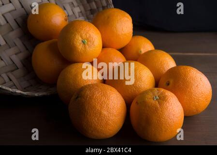 Stillleben, Low-Key oder dunkle Food-Fotografie, Orangen in einem Korb auf einem Tisch Stockfoto