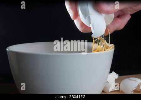 Ein Ei auf einer weißen Schüssel brechen in Frühstück Konzept, schwarzen Hintergrund und Nahaufnahme oder Makro-Fotografie Stockfoto