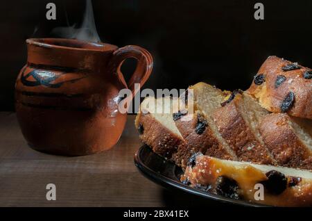 Kuchenscheiben mit Rosinen auf einem schwarzen Teller und einem mexikanischen Ton- oder Schlamm-Kaffeebecher, auf dem Hintergrund auf einem rustikalen Tisch und in einer dunklen Umgebung. Stockfoto