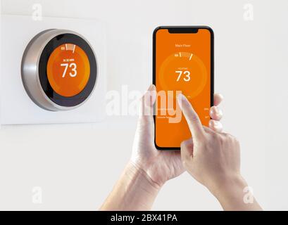 Eine Person, die eine Smartphone-Anwendung verwendet, um die Raumtemperatur mit einem drahtlosen intelligenten Thermostat auf weißem Hintergrund aufzuwärmen. Stockfoto