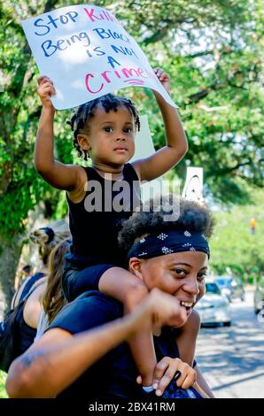 Ein afroamerikanischer Junge hält ein Schild, als er auf den Schultern seiner Mutter bei einem Protest gegen Polizeibrutalität sitzt, 4. Juni 2020, in Mobile, Alabama. Stockfoto