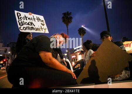 Los Angeles, Kalifornien, USA. Juni 2020. Ein Protestierender hält ein Plakat, das besagt, dass die Schwarze Gemeinschaft beschützt wird, während ein Polizeihubschrauber während der Demonstration hinter ihr fliegt.Demonstranten gingen auf die Straßen Hollywoods, um gegen den Tod George Floyd zu marschieren. Obwohl die Proteste friedlich waren, wurden viele Demonstranten verhaftet, weil sie der Ausgangssperre von Los Angeles nicht gehorchten, die wegen früherer gewalttätiger Proteste und Plünderungen eingerichtet wurde. Kredit: Stanton Sharpe/SOPA Images/ZUMA Wire/Alamy Live News Stockfoto