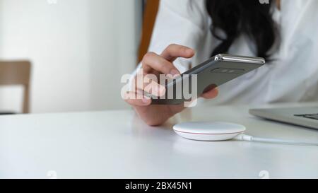 Frau, die im Büro ihr Smartphone auf ein drahtloses Ladegerät setzt Stockfoto