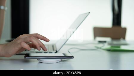 Geschäftsfrau, die am Arbeitsplatz arbeitet und mit einem drahtlosen Gerät Mobiltelefone lädt Stockfoto