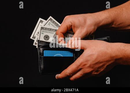 Der Mann auf schwarzem Hintergrund hält eine Geldbörse mit US-Dollar Nahaufnahme.2020 in seinen Händen Stockfoto