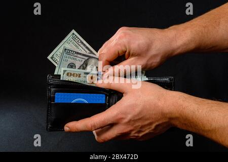 Der Mann auf schwarzem Hintergrund hält eine Geldbörse mit US-Dollar Nahaufnahme.2020 in seinen Händen Stockfoto