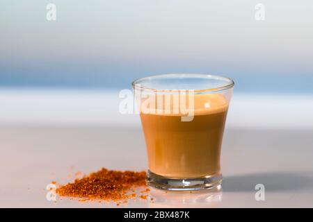Nahaufnahme eines leckeren Cortados neben etwas braunem Zucker auf einem Glastisch auf einem unscharf-hellen Hintergrund. Entspannungs- und Kaffeekonzept. Stockfoto