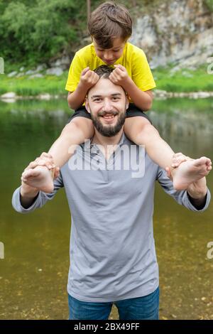 Porträt des jungen Vaters geben Sohn Fahrt auf seinen Schultern. Huckepack Junge hält Papa Haare. Stockfoto