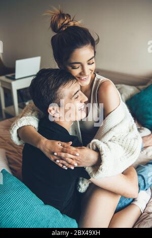 Niedliches kaukasisches Paar umarmt und lächelt, während es auf dem Sofa mit Kissen liegt Stockfoto