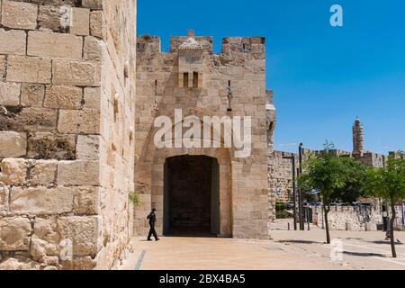 Ein einjähriger maskierter Polizist, der während der Quarantäne am jaffa-Tor der Altstadt jerusalems mit dem Turm davids im Hintergrund vorbeigeht Stockfoto