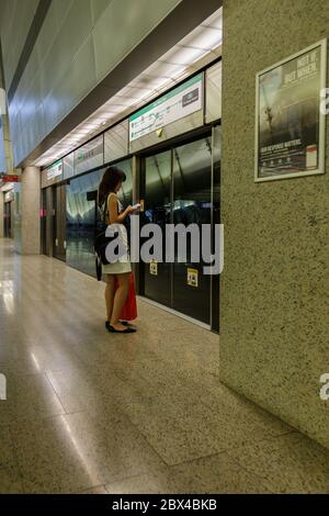 Singapur - 07. Juli 2017: Nicht identifizierter Mann mit Rucksack, der Smartphone spielt, während er auf den MRT-Zug wartet, der zur Plattform in Singapur kommt. Stockfoto
