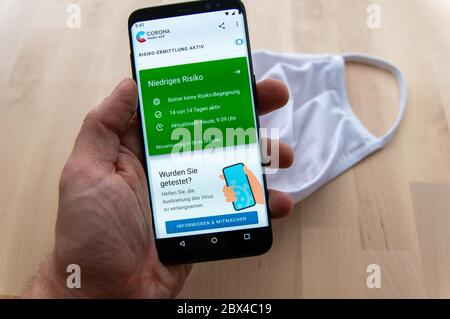 Zittau, Sachsen / Deutschland - 5. Juni 2020: HandSmartphone mit aktiver Risikoanalyse der deutschen Corona Warn App mit verschwommener weißer Gesichtsmaske Stockfoto