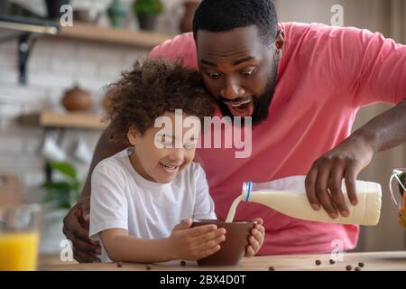 afroamerikanischer bärtiger Mann, der Milch in seinen Töchterteller gießt Stockfoto
