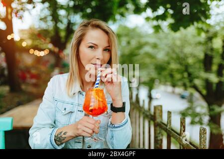 Junge Frau, die italienischen Cocktail trinkt - Aperol Spritz. Feine Struktur der Filmkörnung. Stockfoto