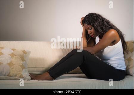 Junge attraktive und traurige schwarze afroamerikanische Frau sitzt depressiv zu Hause Sofa Couch Gefühl ängstlich und frustriert Leiden Depression Problem Stockfoto