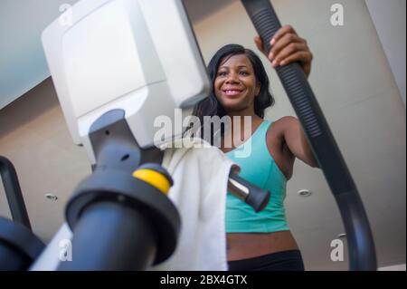 Lifestyle-Fitness-Studio Porträt von jungen attraktiven und glücklichen schwarzen afroamerikanischen Frau Training im Fitness-Club lächelnd fröhlich und schwitzend während elliptisch Stockfoto