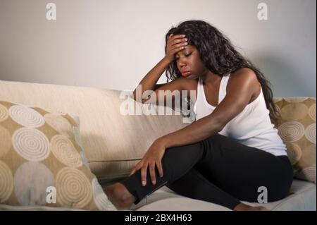 Junge attraktive und traurige schwarze afroamerikanische Frau sitzt depressiv zu Hause Sofa Couch Gefühl ängstlich und frustriert Leiden Depression Problem Stockfoto