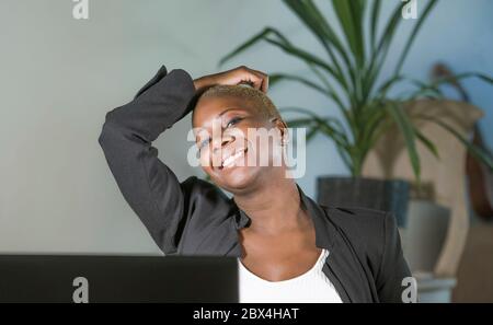 Junge glückliche und erfolgreiche schwarze Afro amerikanische Frau lehnt auf Bürostuhl aufgeregt und freudig arbeiten am Laptop-Computer-Schreibtisch an modernen Arbeitsplatz in Stockfoto