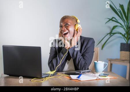 Junge glückliche schwarze Afro amerikanische Frau Musik mit Kopfhörern hören aufgeregt und freudig arbeiten am Laptop-Computer-Schreibtisch an einem modernen Arbeitsplatz im Bus Stockfoto