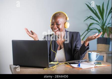 Junge glückliche schwarze Afro amerikanische Frau Musik mit Kopfhörern hören aufgeregt und freudig arbeiten am Laptop-Computer-Schreibtisch an einem modernen Arbeitsplatz im Bus Stockfoto